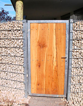 eine besondere Grundstückseinfassung bietet ein Gabionenzaun mit einem Holztor in Metallrahmen